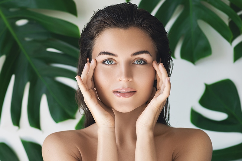 Portrait of young and beautiful woman with perfect smooth skin in tropical leaves. Concept of natural cosmetics and skincare.