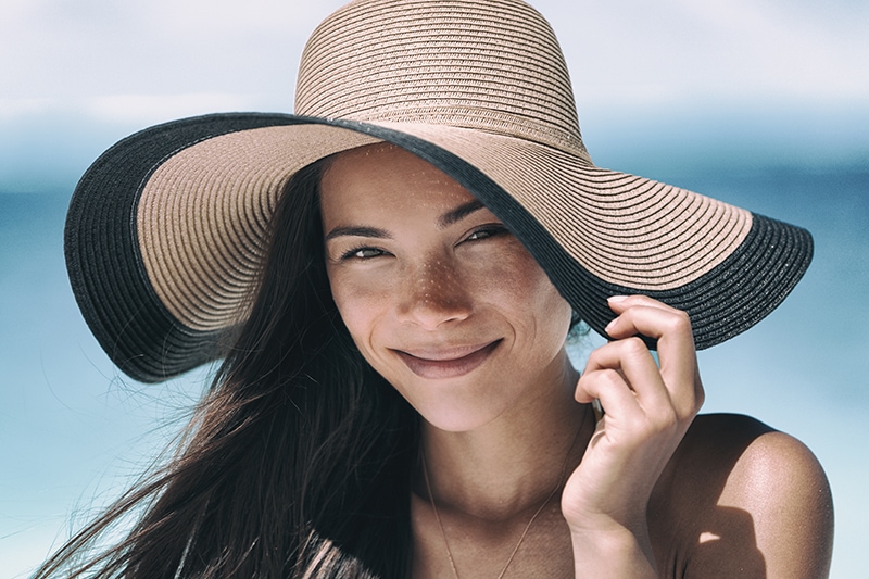 Beach sun tan skin care Asian beauty woman happy on beach vacation panoramic banner wearing sunhat. Healthy suntan skincare concept with hat.